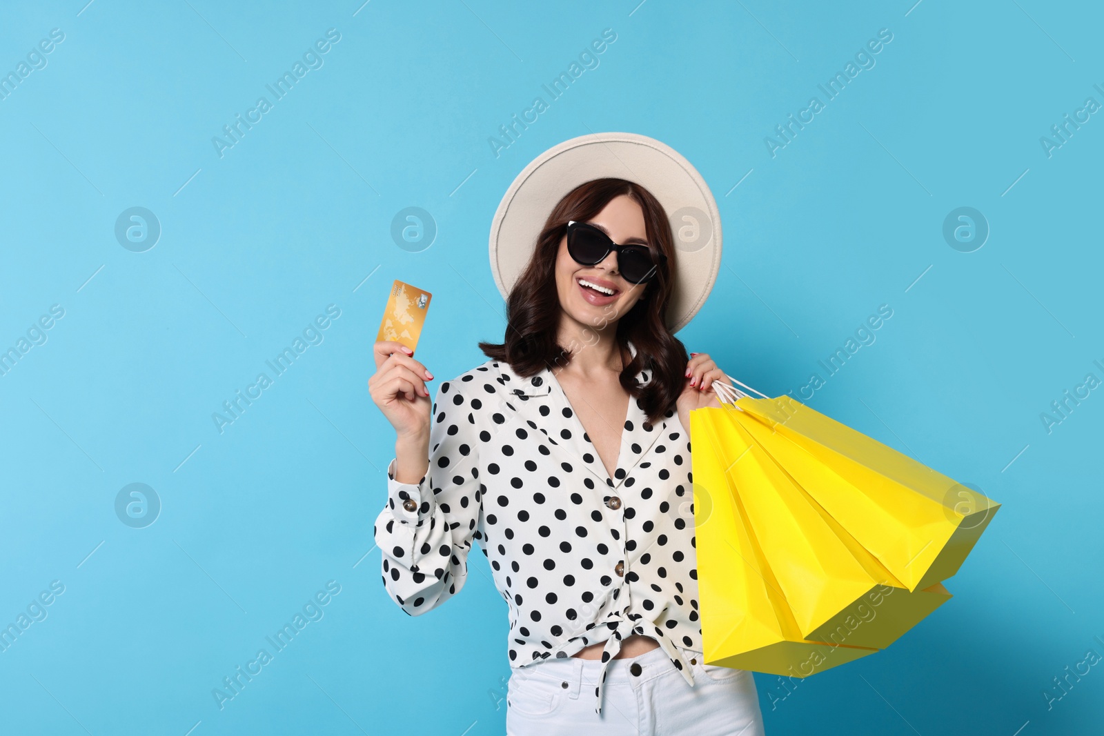 Photo of Beautiful young woman with paper shopping bags and credit card on light blue background