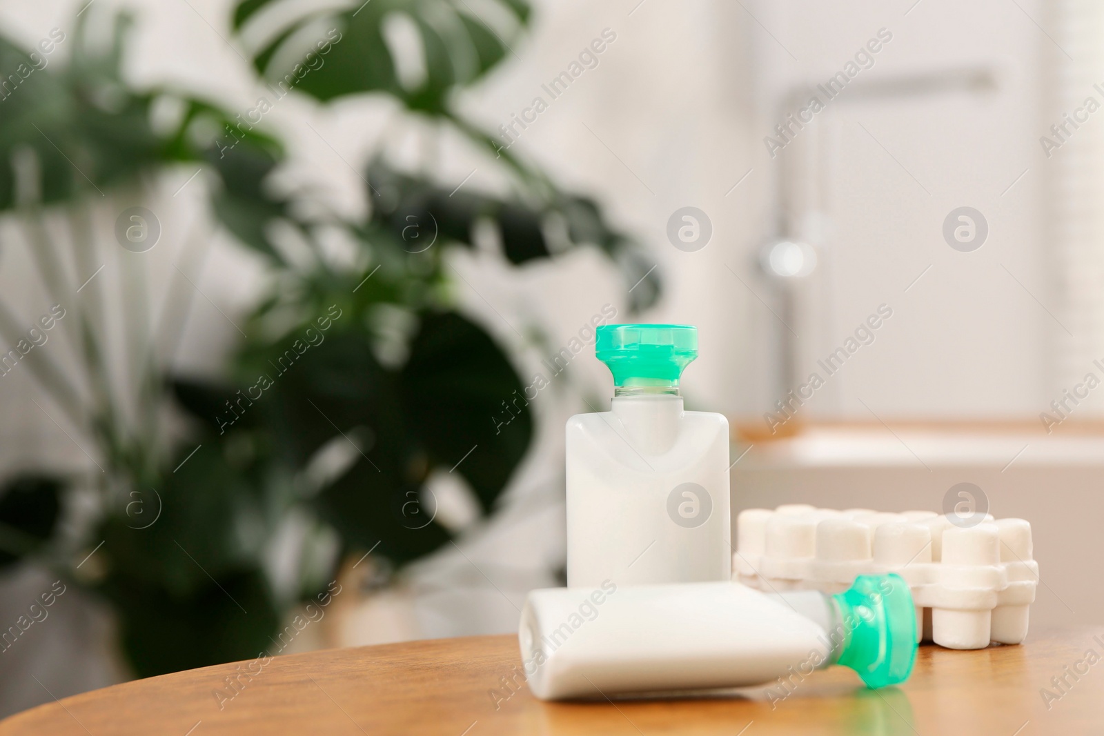 Photo of Mini bottles of cosmetic products and soap on wooden table against blurred background. Space for text