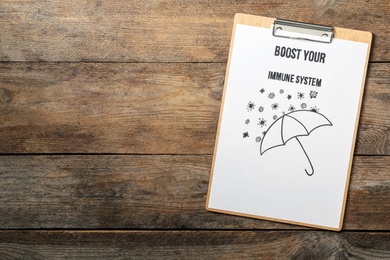 Clipboard with phrase Boost Your Immune System on wooden table, top view. Space for text