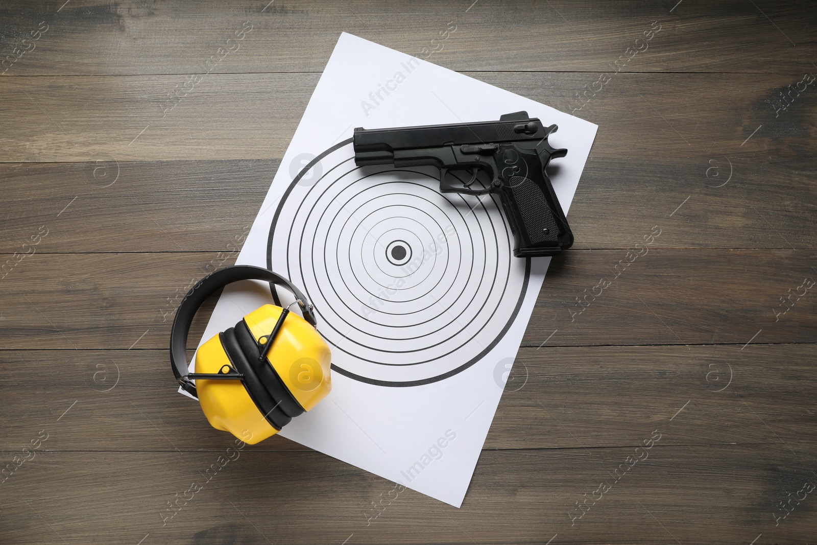 Photo of Shooting target, handgun and headphones on wooden table, top view