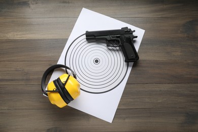 Shooting target, handgun and headphones on wooden table, top view