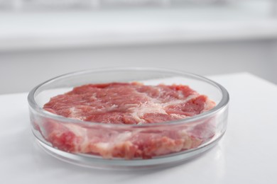 Photo of Petri dish with piece of raw cultured meat on white table indoors, closeup