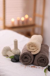 Spa stones, rolled towels and herbal bags on massage table indoors