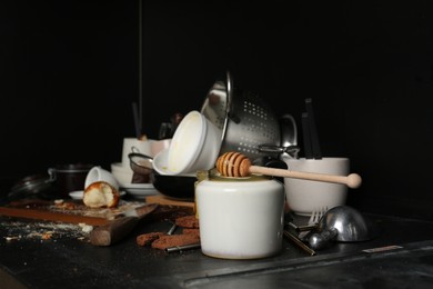 Many dirty utensils, dishware and food leftovers on black countertop. Mess in kitchen