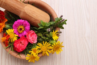 Mortar with pestle and beautiful fresh flowers on wooden table, top view. Space for text