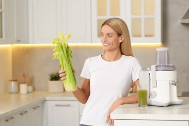 Photo of Happy woman with fresh celery bunch at table in kitchen