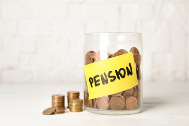 Photo of Coins in glass jar with label "PENSION" on table against light wall