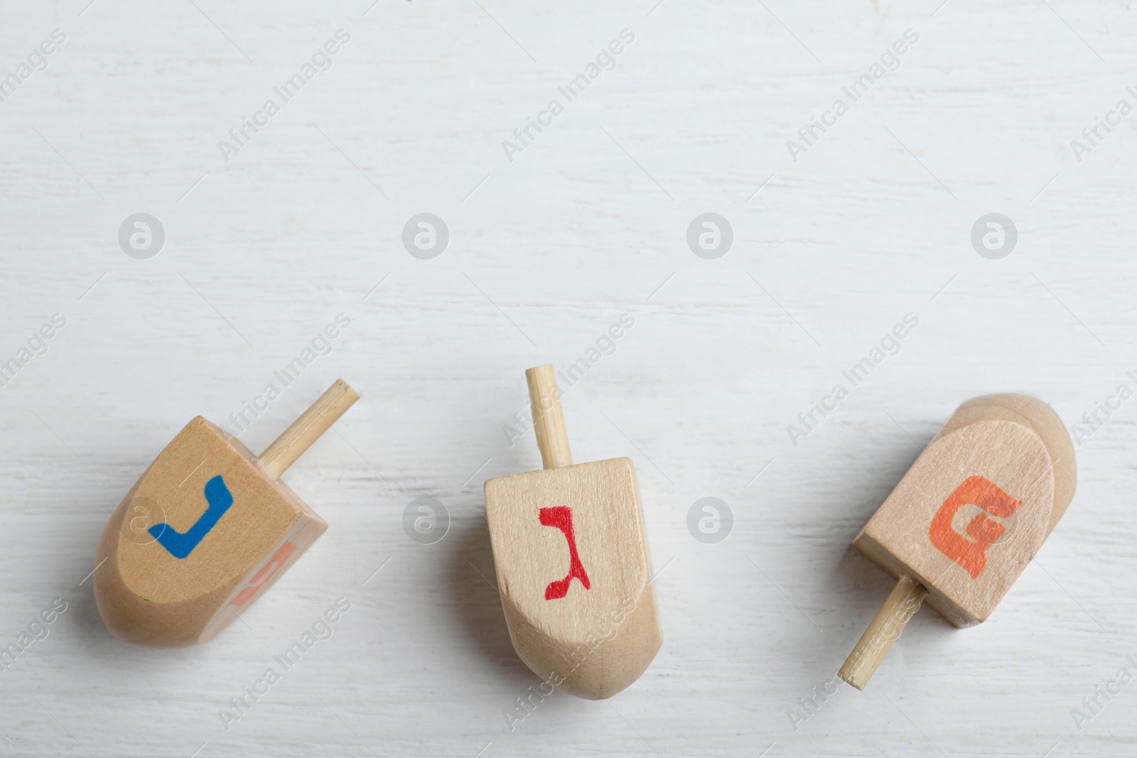 Photo of Hanukkah traditional dreidels with letters Nun, Gimel and He on white wooden table, flat lay. Space for text
