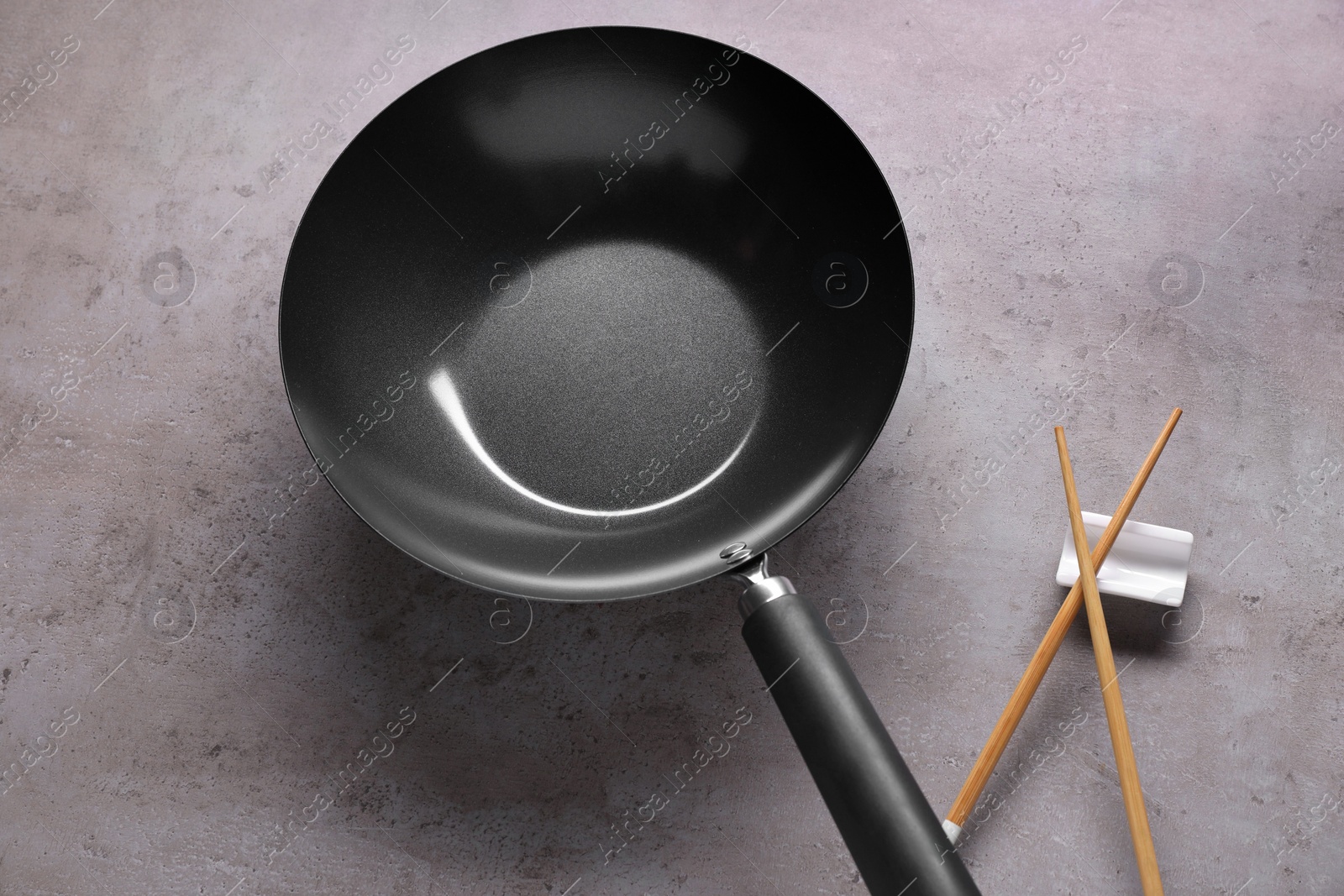 Photo of Empty iron wok and wooden chopsticks on grey table