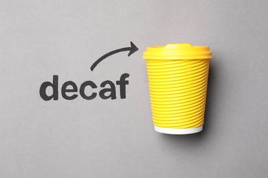 Photo of Word Decaf and arrow pointing at takeaway paper coffee cup on light grey background, top view