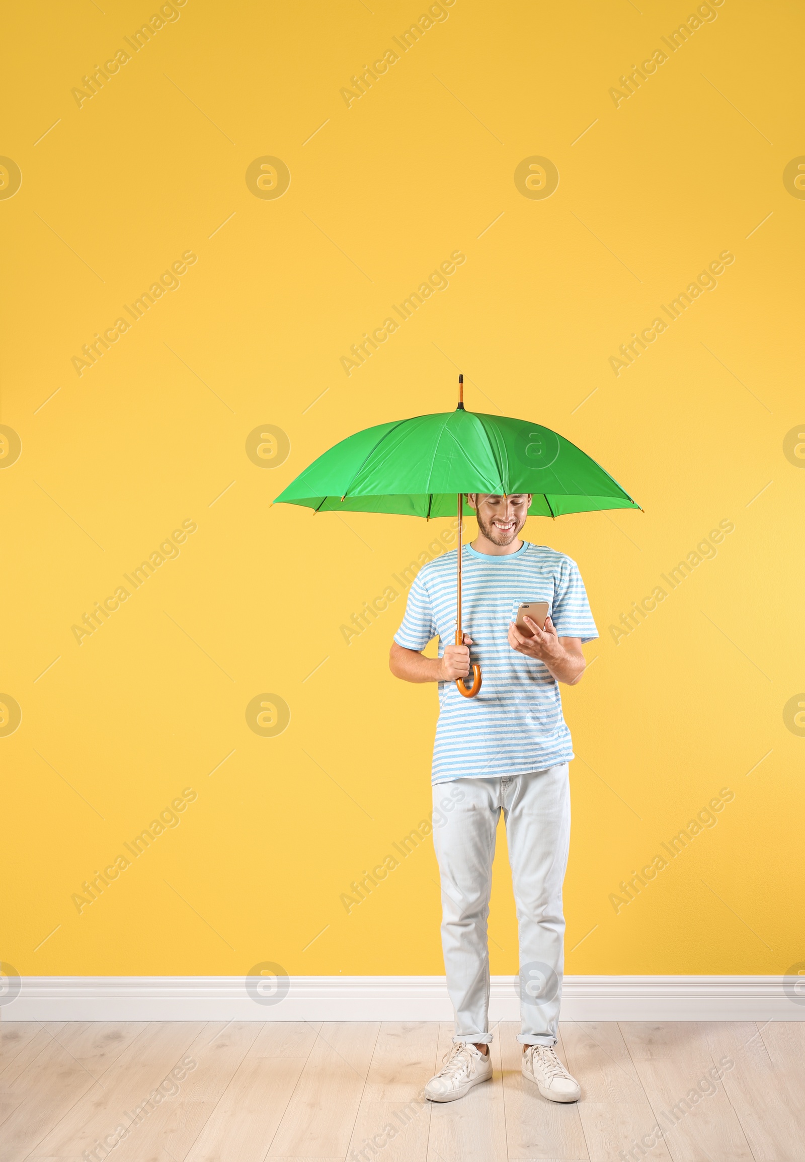 Photo of Man with green umbrella and smartphone near color wall