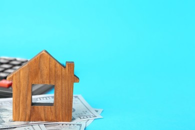 Photo of Wooden house model, money and calculator on light blue background, space for text. Mortgage concept