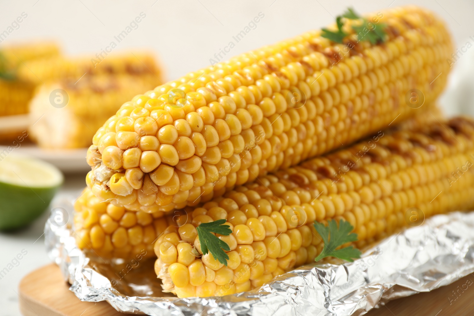 Photo of Tasty grilled corn on wooden board, closeup