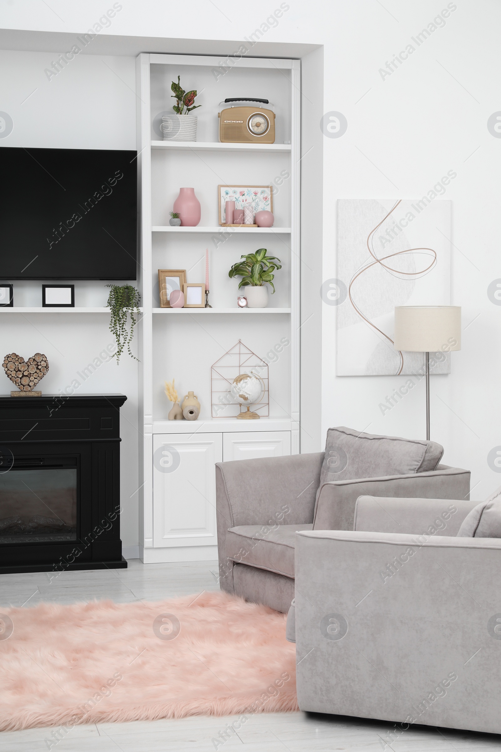 Photo of Stylish room interior with beautiful fireplace, TV set, armchairs and shelves with decor
