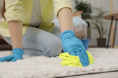 Photo of Woman in rubber gloves cleaning carpet with rag indoors, closeup