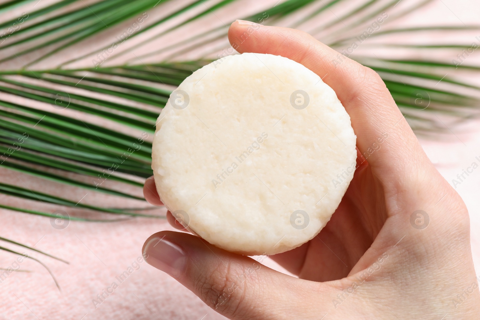 Photo of Woman holding solid shampoo bar at pink table, closeup. Hair care