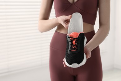 Photo of Sporty woman putting orthopedic insole into shoe indoors, closeup. Foot care