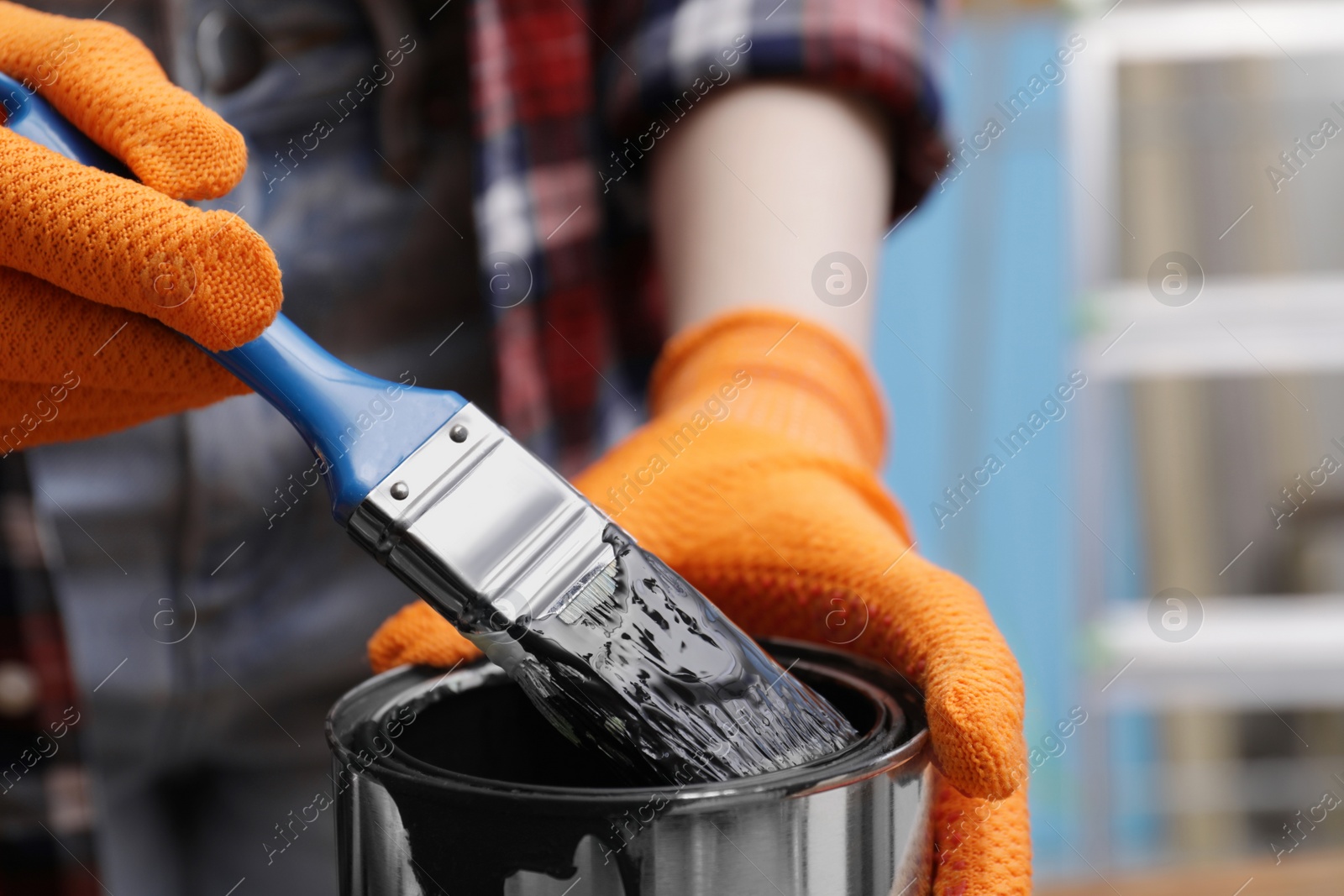 Photo of Woman dipping brush into can of black paint indoors, closeup