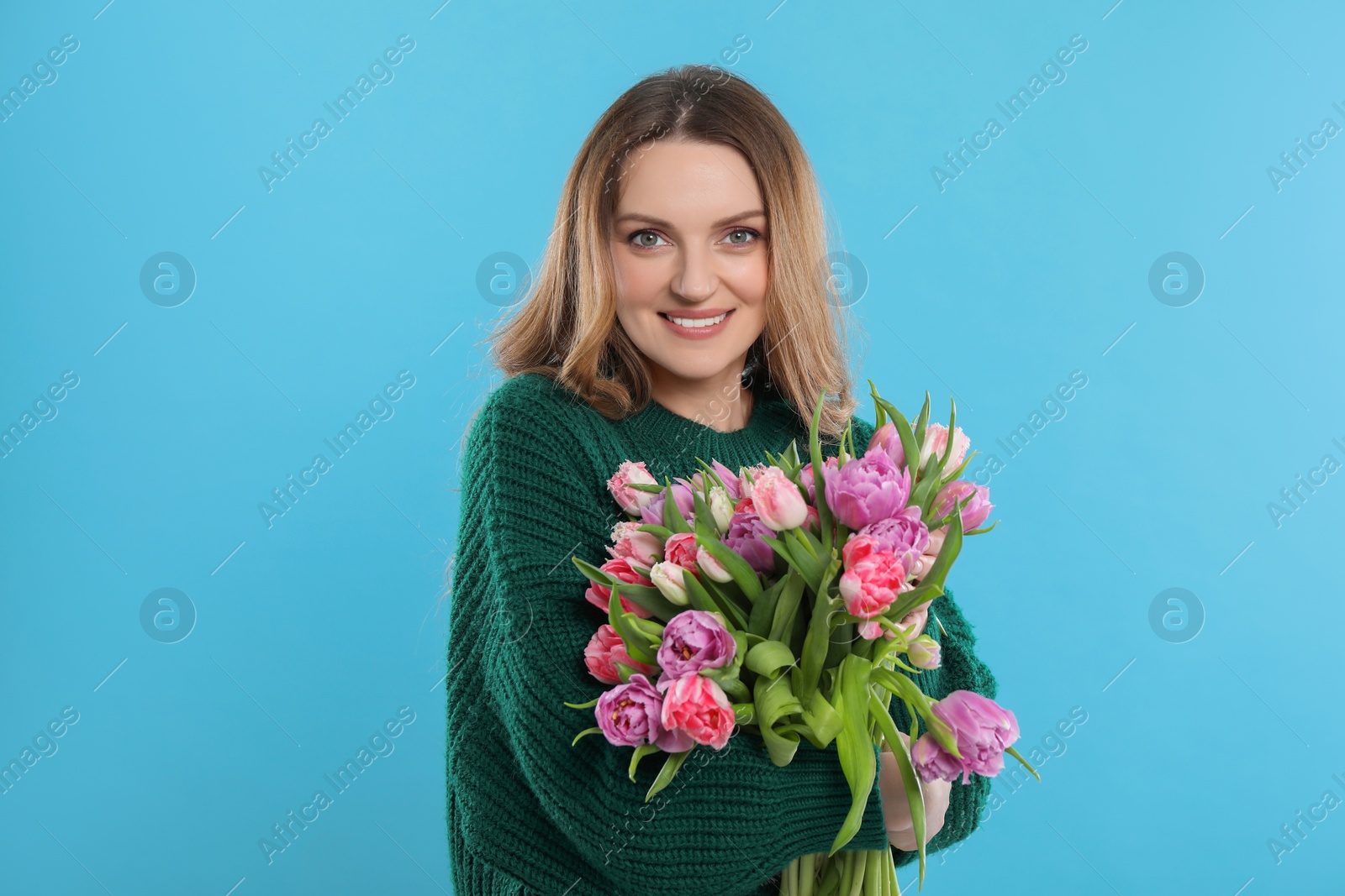 Photo of Happy young woman with bouquet of beautiful tulips on light blue background