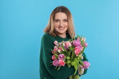 Happy young woman with bouquet of beautiful tulips on light blue background