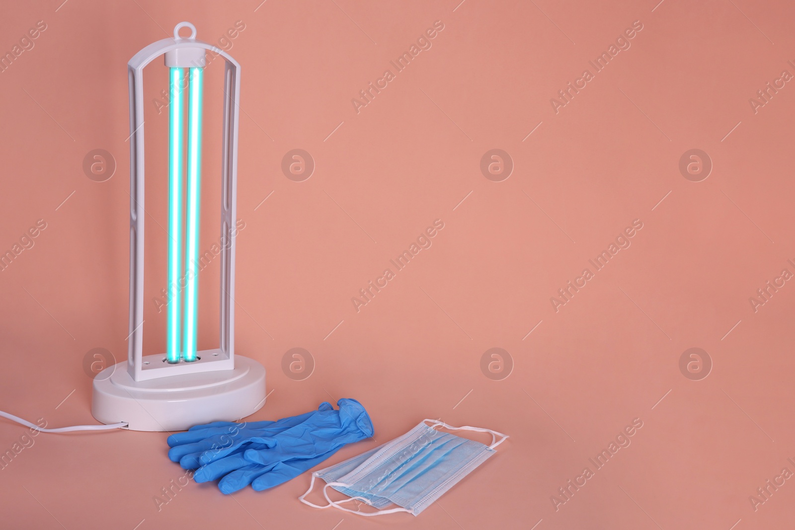 Photo of Ultraviolet lamp, medical masks and gloves on peach background, space for text
