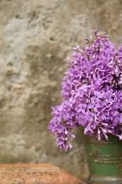 Beautiful lilac flowers in bucket near stone wall, space for text