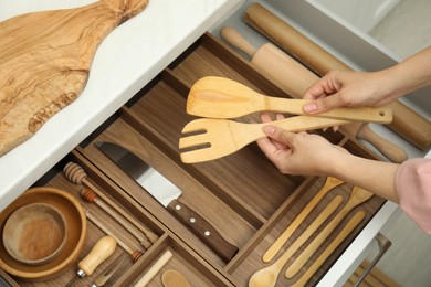 Woman taking wooden spatula and fork from open drawer of kitchen cabinet, above view