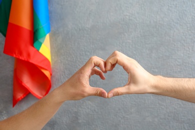 Gay couple making heart symbol with hands near rainbow flag