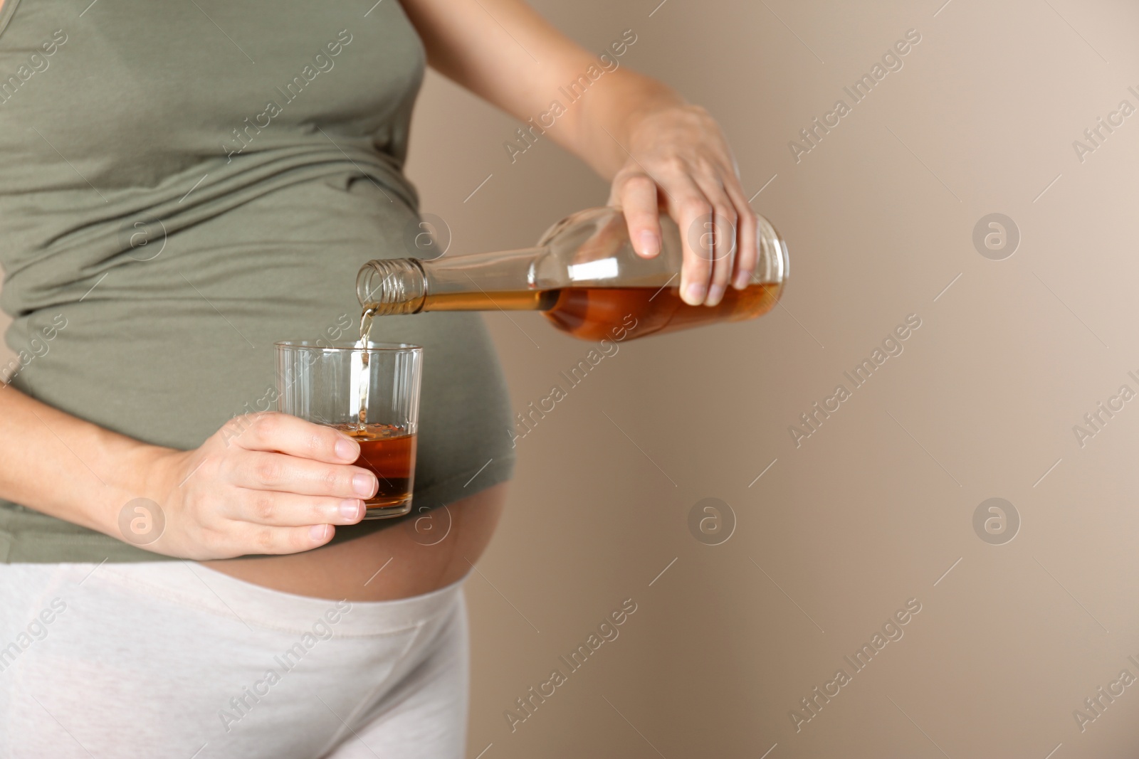 Photo of Pregnant woman pouring whiskey into glass on color background, space for text. Alcohol addiction