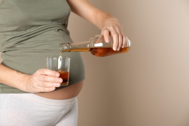 Photo of Pregnant woman pouring whiskey into glass on color background, space for text. Alcohol addiction