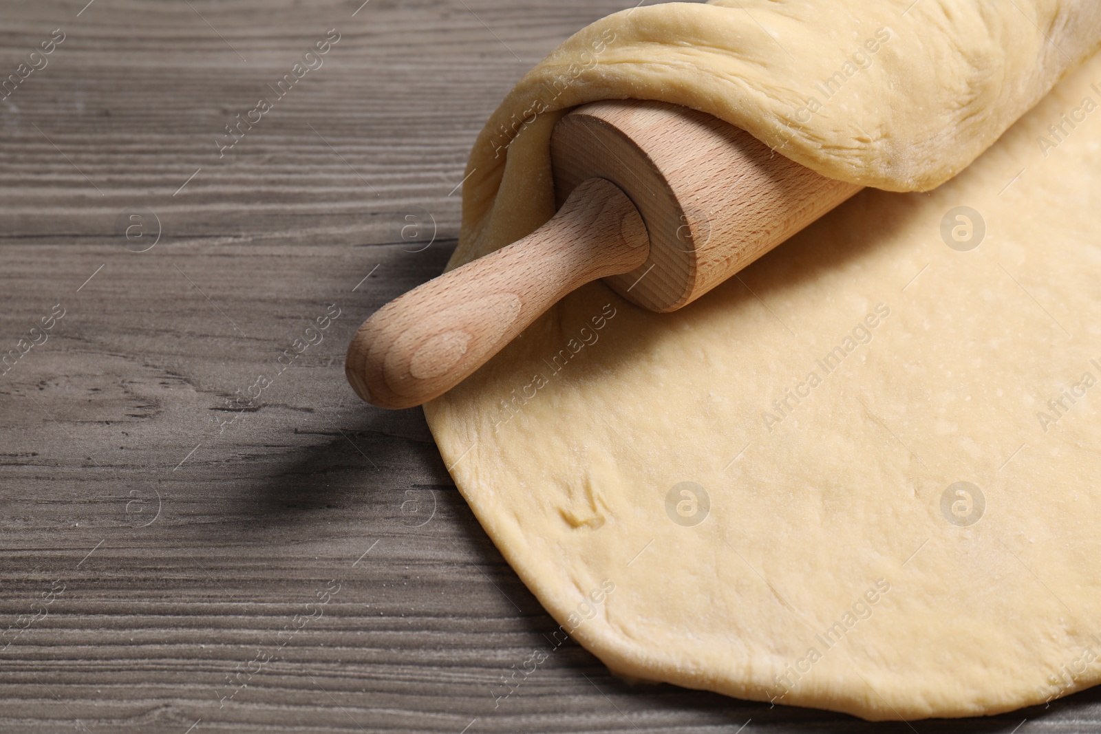 Photo of Raw dough and rolling pin on wooden table, space for text