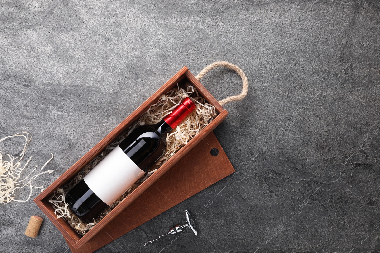 Photo of Bottle of wine in wooden box and corkscrew on dark textured table, flat lay. Space for text