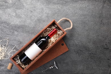 Bottle of wine in wooden box and corkscrew on dark textured table, flat lay. Space for text