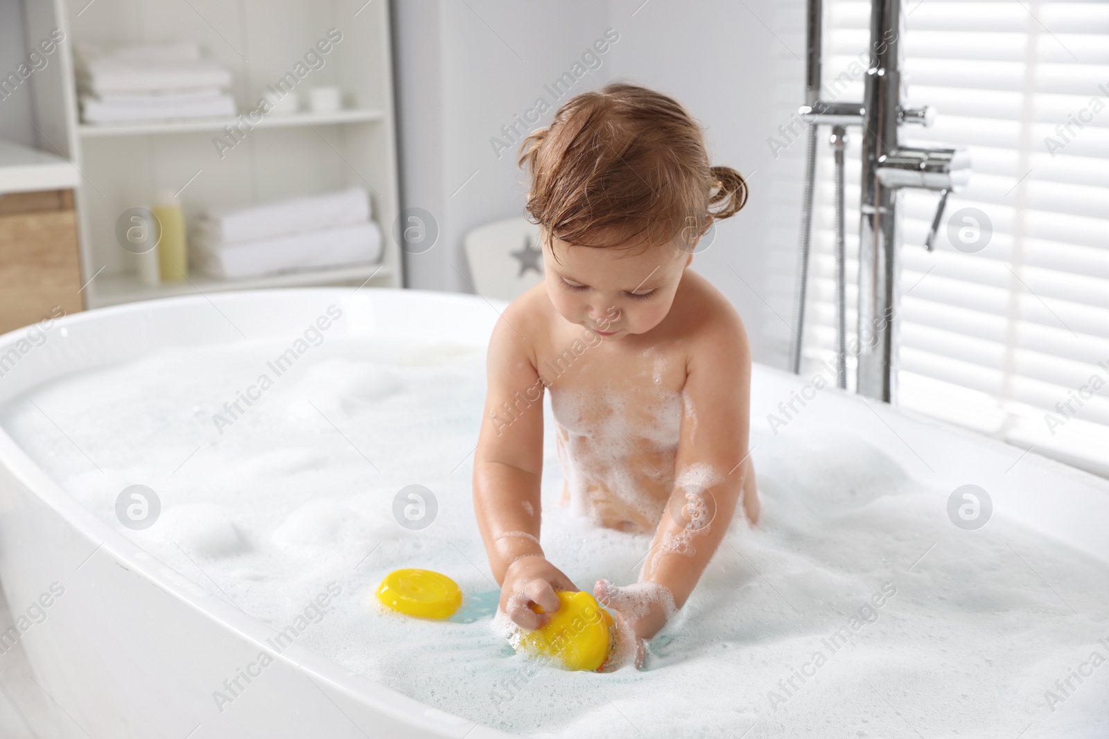 Photo of Cute little girl with rubber ducks in foamy bath at home