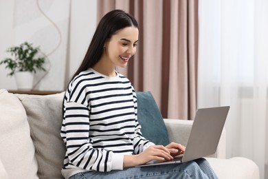 Photo of Happy young woman using laptop on sofa at home
