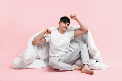 Photo of Happy man in pyjama with sleep mask and blanket on pink background