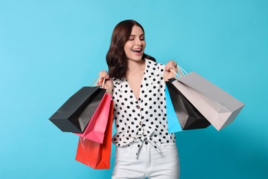 Beautiful young woman with paper shopping bags on light blue background