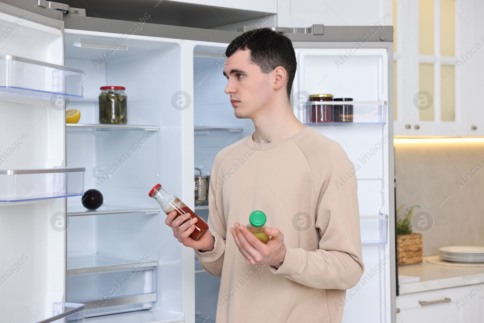 Photo of Upset man with sauces near empty refrigerator in kitchen