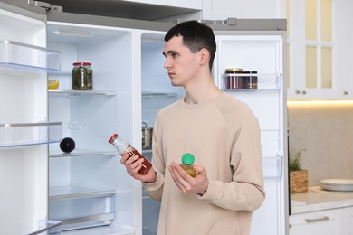 Upset man with sauces near empty refrigerator in kitchen