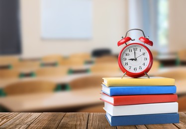 Image of Red alarm clock and different books on wooden table in classroom, space for text