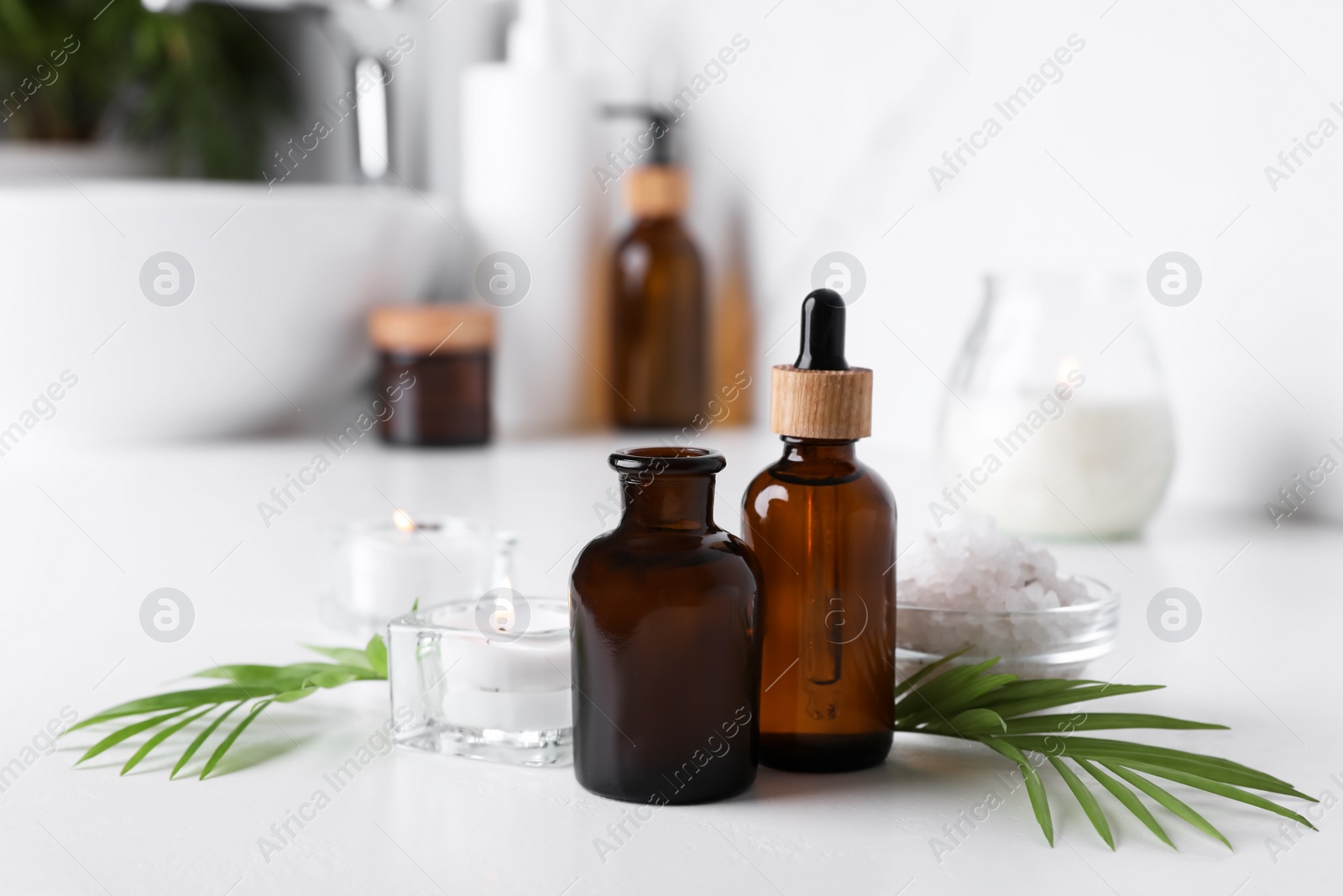 Photo of Essential oils, sea salt and candles on white table in bathroom, closeup