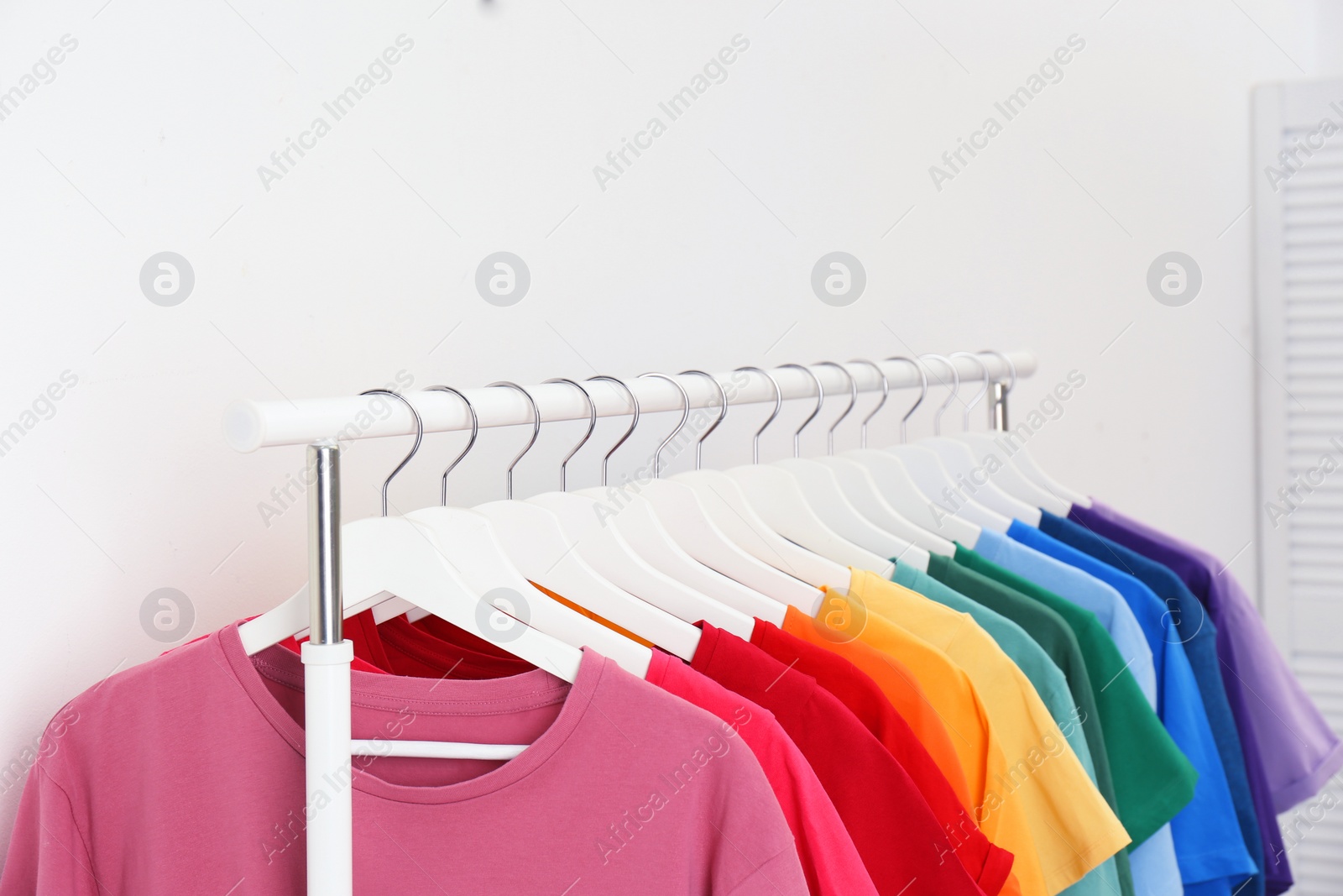 Photo of Rack with bright clothes in room. Rainbow colors