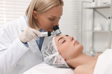 Dermatologist with dermatoscope examining patient`s face in clinic