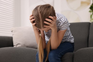 Photo of Little girl suffering from headache on sofa indoors