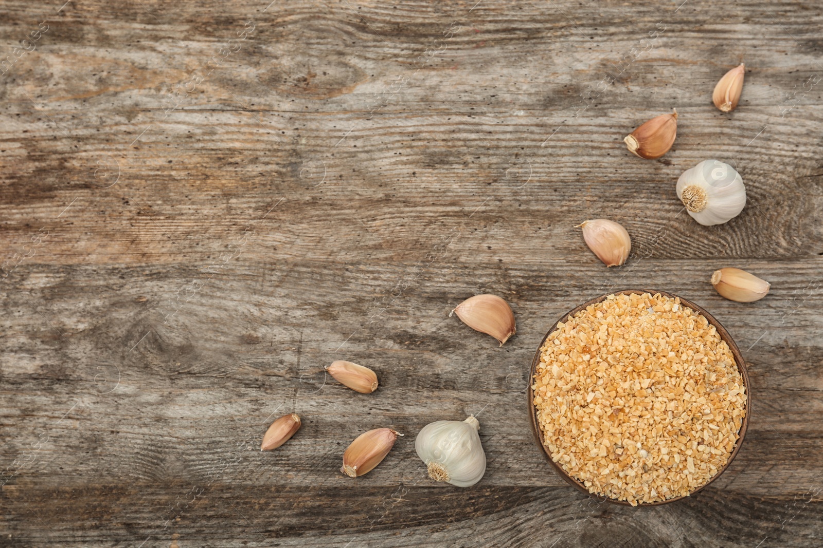 Photo of Bulbs, cloves and bowl with granulated dried garlic on wooden table, top view