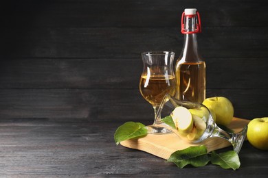 Delicious cider and apples with green leaves on black wooden table, space for text