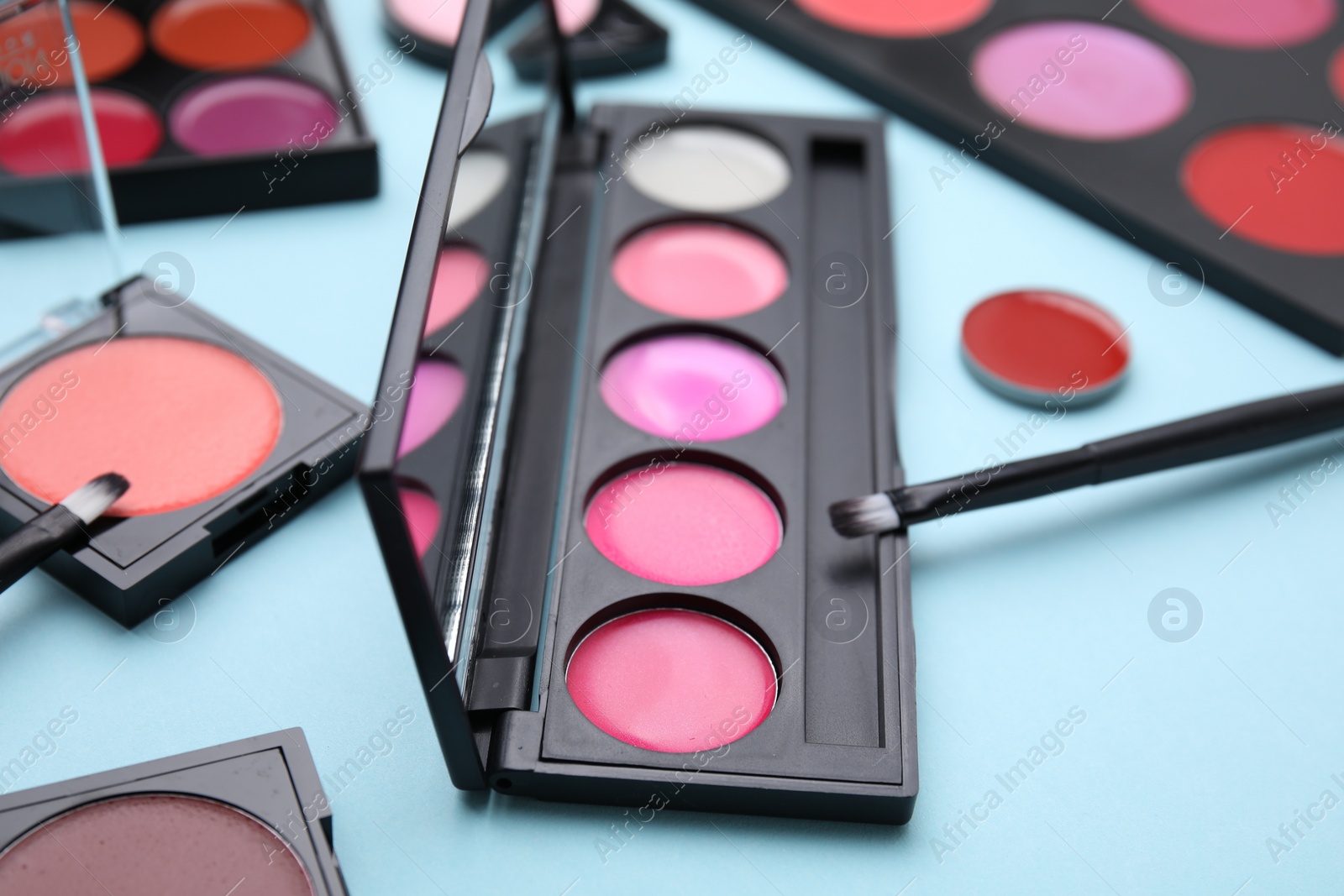 Photo of Colorful lip palettes and brushes on light turquoise background, closeup