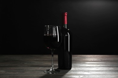 Glass and bottle of red wine on wooden table against black background