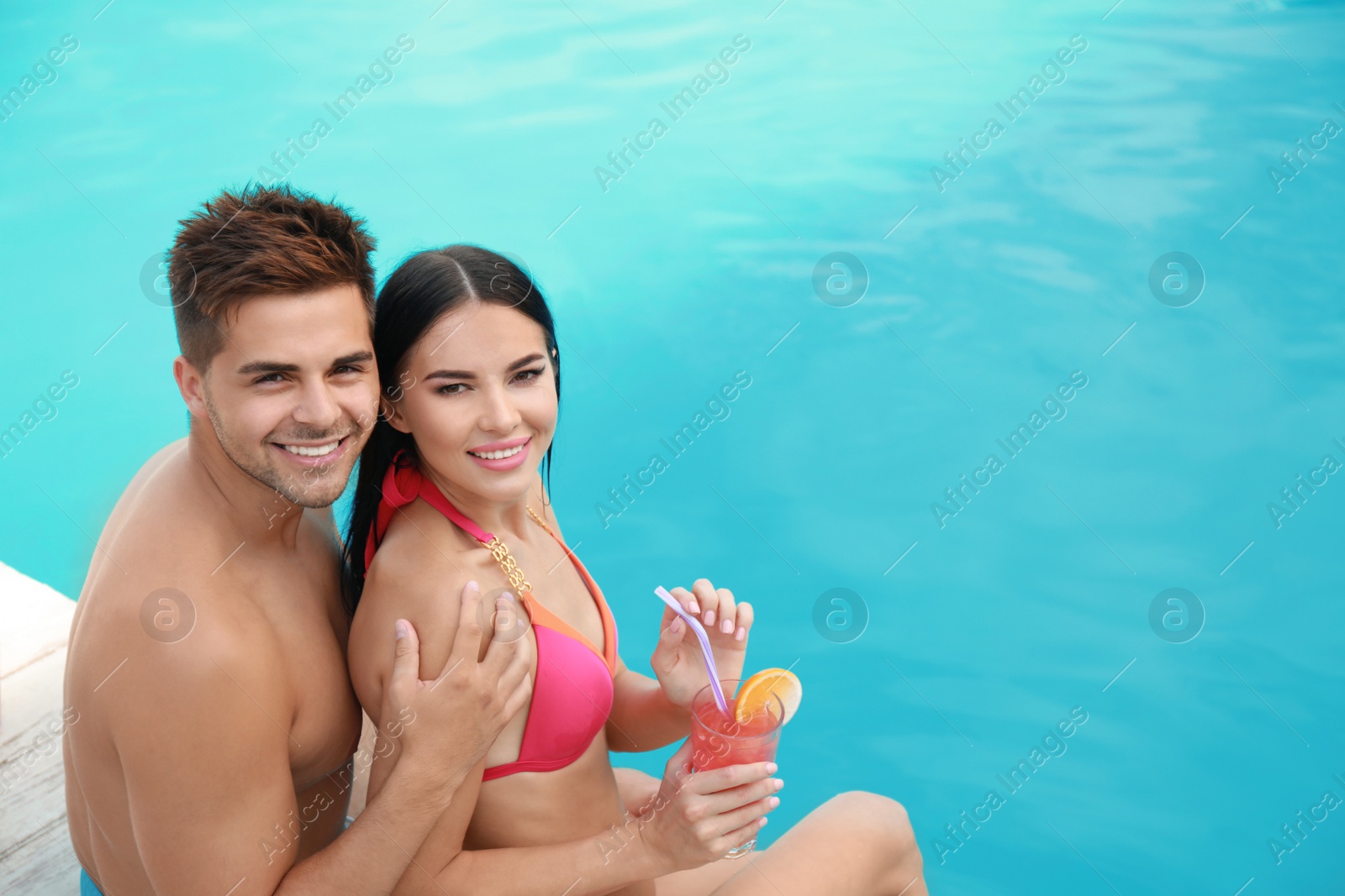 Photo of Woman in bikini with boyfriend near outdoor pool. Happy young couple