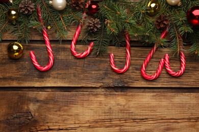 Photo of Flat lay composition with tasty candy canes and Christmas decor on wooden table, space for text